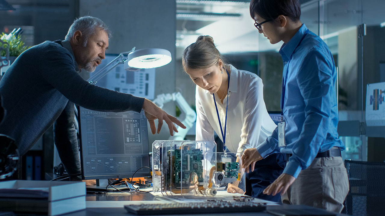 Team of Computer Engineers Lean on the Desk and Choose Printed Circuit Boards